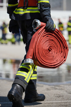 Firefighter Carrying Rolled Fire Hose In Safety Gear At Emergency Training Scene
