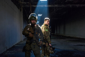 Obraz premium Two Soldiers in Tactical Gear Standing Back-to-Back in Dark Urban Military Interior
