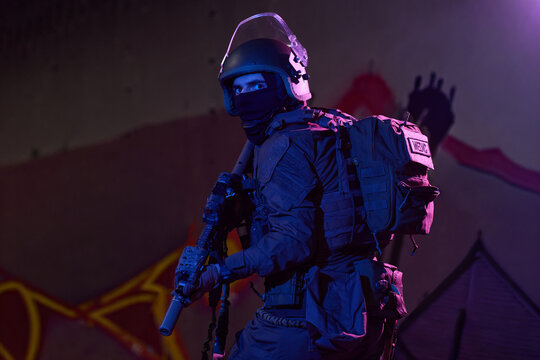 Tactical Medic Soldier In Night Urban Raid Wearing Helmet, Balaclava, Tactical Gear And Rifle
