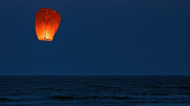 Glowing lantern ascends over dark ocean under night sky