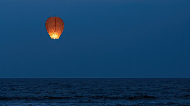 Orange lantern ascends over calm ocean at dusk