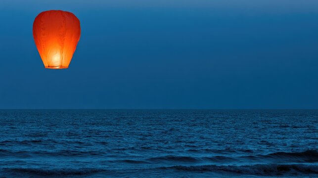 Glowing lantern ascends over calm ocean at twilight