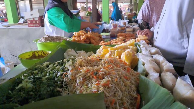 Traditional Indonesian market vendor preparing Urap vegetables for customer. Colorful mixed vegetables with grated coconut served on banana leaf. Healthy traditional jajanan pasar, local market food.