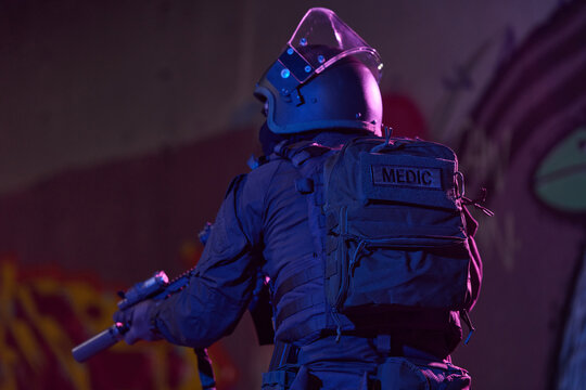 Tactical Medic Officer in Riot Gear With Helmet and Medical Backpack at Night Operation