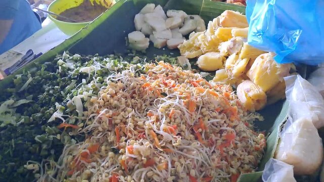 Traditional Indonesian market vendor preparing Urap vegetables for customer. Colorful mixed vegetables with grated coconut served on banana leaf. Healthy traditional jajanan pasar, local market food.