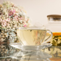 Obraz premium Glass teapot with herbal tea and flowers on a table, bright home interior. Tea relaxation, wellness, herbal, cozy, indoors