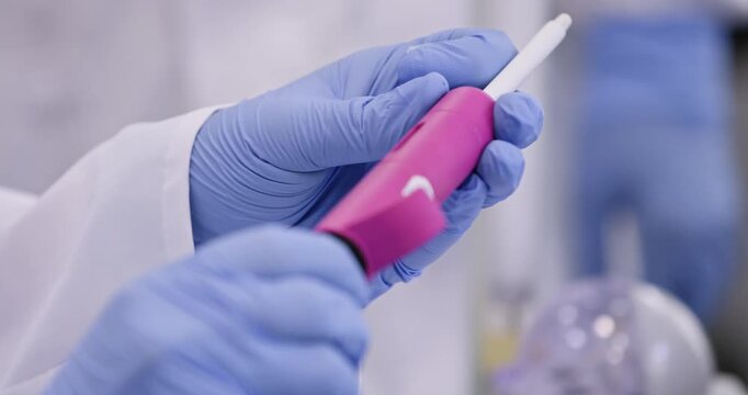 A man in a white coat and blue gloves sets the working volume on the dispenser and takes a small test tube with DNA in his hand, close-up.