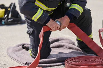 Fotobehang Sportwinkel Firefighter Connecting Red Fire Hose During Training Drill in Protective Turnout Gear on Pavement  © .shock