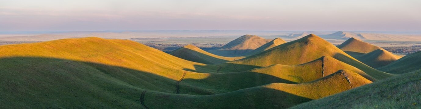 Panoramic landscape view. Summer sunset at Hills in the Orenburg region, Russia. Hilly terrain, mountain fields. The beginning of the Ural Mountains.