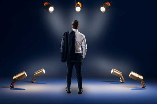 Businessman Standing Under Studio Spotlights, Facing a Bright Opportunity in a Dramatic Dark Background, Leadership and Decision Concept.