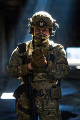 Obraz premium Armed Soldier in Camouflage Tactical Gear With Rifle and Helmet Standing in Dim Light