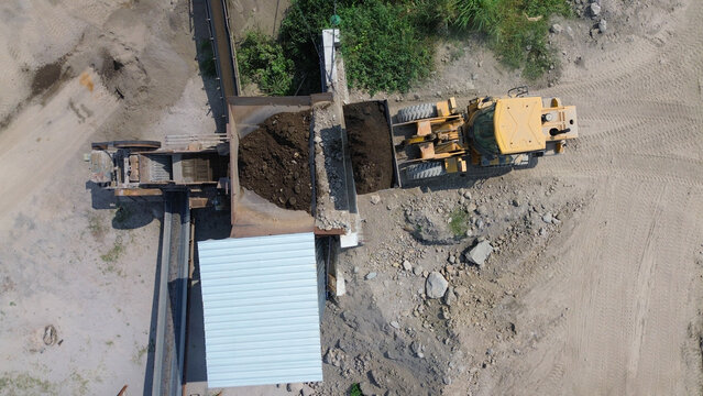 Top view aerial of wheel loader feeding raw material into stone crusher hopper at aggregate processing plant