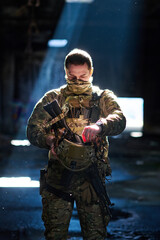 Fototapeta premium Tactical Soldier In Camouflage Gear Holding Helmet And Rifle Under Dramatic Light In Abandoned Building