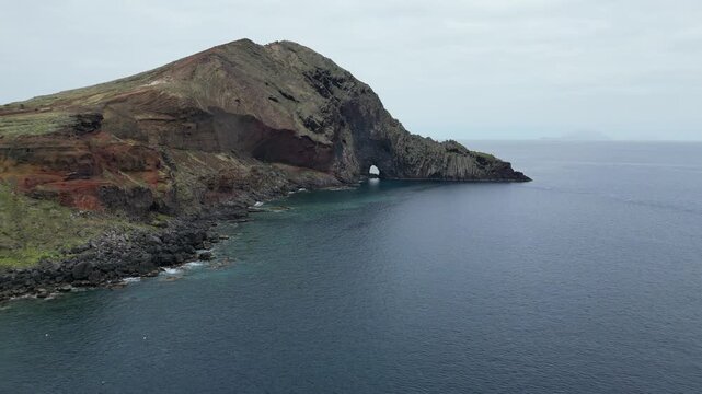 Drone aerial push forward shot of spectacular natural rock arch in volcanic Madeira cape