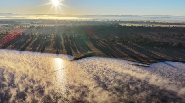 Aerial video of Lake Keepit Dam blanketed by morning fog in NSW, Australia. Low cloud drifts across the reservoir and surrounding landscape