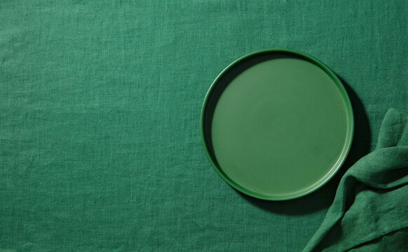 Empty green plate on matching linen tablecloth background. Copy space. Top view.
