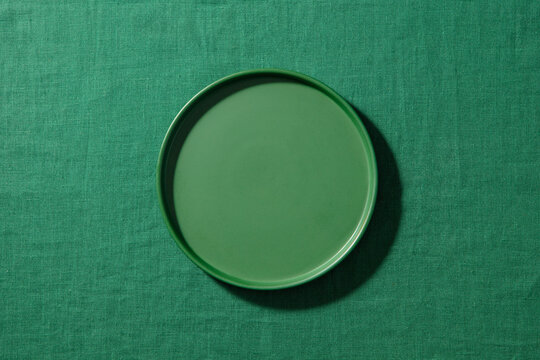 Empty green matte plate on green fabric background. Close up, copy space, top view.
