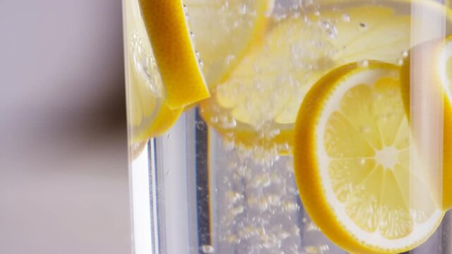Slow motion close up pan of lemon slices fizzing in glass of sparkling water on neutral indoor countertop