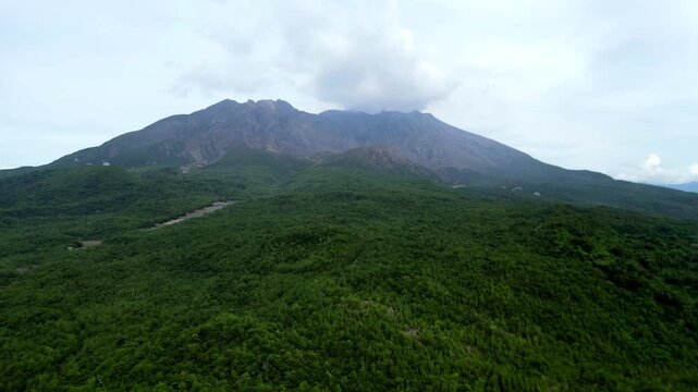 Cinematic aerial drone footage flying towards the majestic, active stratovolcano of Sakurajima, showcasing its rugged summit and volcanic slopes rising above Kagoshima Bay, Japan