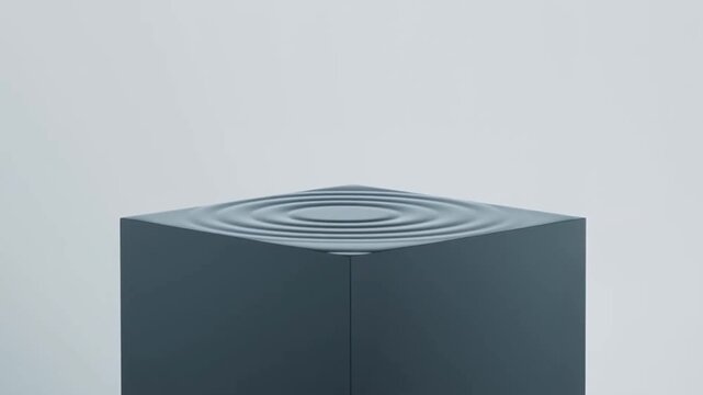Slow motion static close up of water droplet impacting top of dark cube producing concentric ripples and surface depression on glossy pedestal in minimal grey studio interior