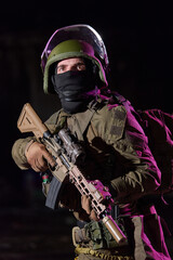 Fototapeta premium Armed Soldier In Tactical Gear With Rifle And Helmet Standing Alert In Low Light