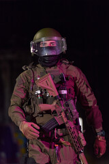 Fototapeta premium Armed Tactical Soldier In Riot Gear With Helmet Visor And Rifle Standing Alert At Night