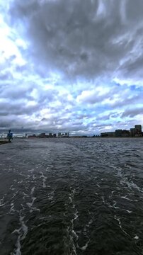 Wide Angle View of Open Water and Dynamic Cloudy Sky Over IJ River Waterfront in Amsterdam with Distant City Skyline