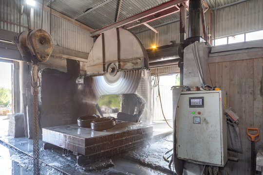 Industrial circular saw machine cutting granite block with automated CNC control panel in a stone processing factory