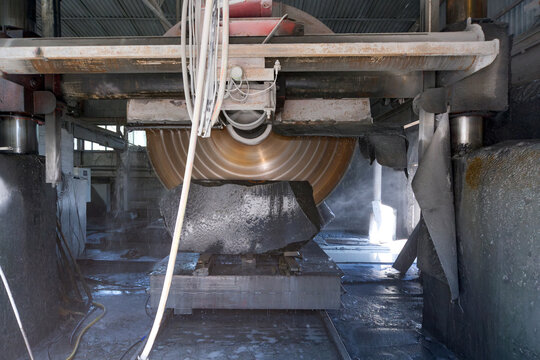 Heavy industrial circular saw machine cutting a large granite stone block at a manufacturing factory
