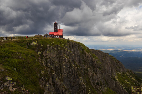 Mountain cottage with a red roof on a rocky cliff under dramatic storm clouds in Karkonosze National Park, Poland