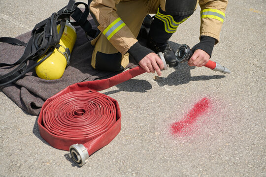 Firefighter Kneeling Connecting Red Fire Hose to Nozzle Beside Air Tank During Drill
