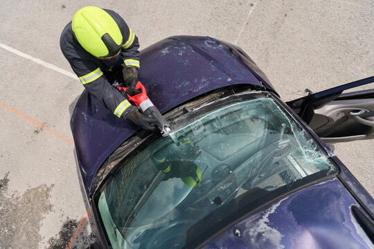 Firefighter Performing Vehicle Rescue Extraction With Hydraulic Cutter On Crashed Car Windshield