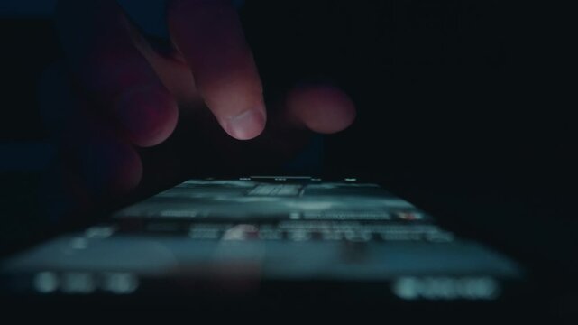 Smartphone news feed browsing at night in macro. Close up male finger scrolling a glowing display. Smartphone usage reflects digital news addiction social media habits and constant mobile connection