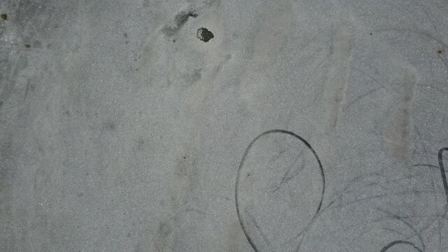 Tire marks and a circular patch on a gravel surface in the afternoon light