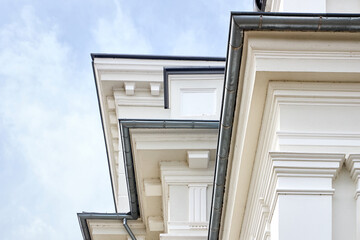 Exterior wall of Holy Trinity Church in Indura features ornate neoclassical plaster details, white decorative moldings, and gray drainage gutters under a light cloudy summer sky. © R_Yosha