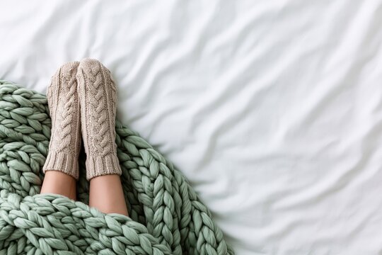 Cozy feet in wool socks under a knitted blanket for winter comfort on a bed morning