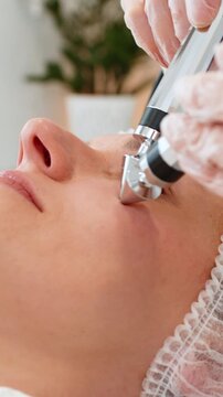 Beautician in gloves uses microcurrent electrodes near eyes and nose of Caucasian woman in beauty clinic. Client relaxes during noninvasive anti age facial therapy for smoother fresh skin care result.