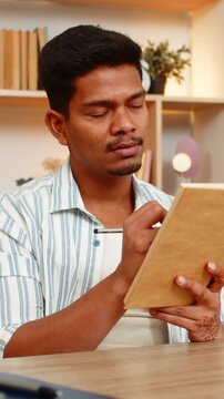Indian man on home table reads book makes notes and pauses to think during focused study indoors at home. Arabian boy on home table reviews pages and writes ideas for learning planning and home work.