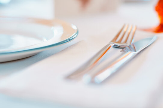 Close-up of an elegant table setting featuring a white plate and polished cutlery on a linen tablecloth, conveying fine dining, hospitality, minimal style and a calm, sophisticated atmosphere.