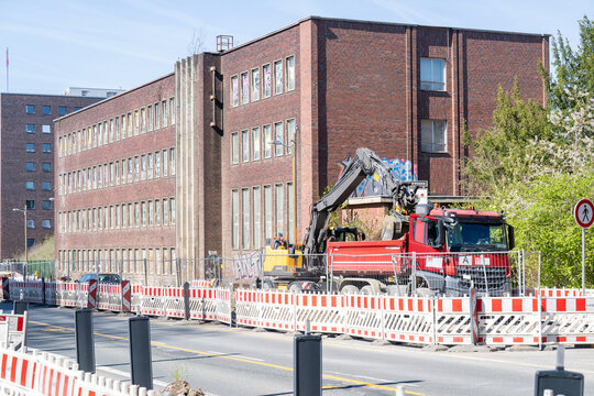 Bagger bel&auml;dt Kipplaster auf einer abgesperrten Stra&szlig;enbaustelle