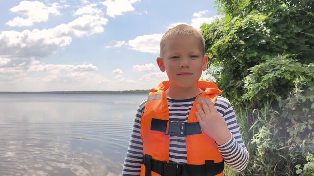 A toddler in a bright orange life jacket stands by the calm water, highlighting essential child water safety and the peace of mind that proper gear brings to family outings near lakes and rivers.