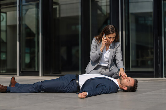 Woman calling ambulance for unconscious man lying on floor. Employee helping colleague who fainted in office building. First aid at work, emergency situation and health care crisis.