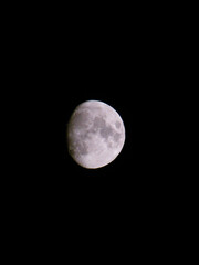 Fototapeta premium Primer plano de la Luna gibosa creciente sobre un cielo nocturno completamente negro, destacando sus cráteres y mares lunares con gran nivel de detalle.