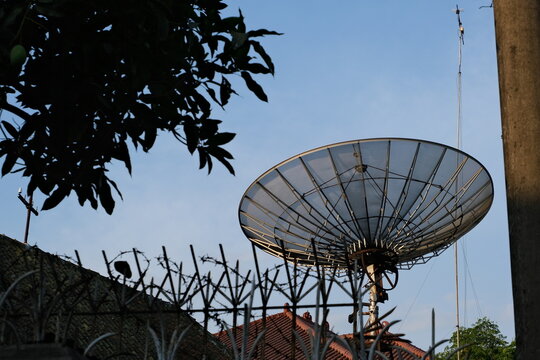 Large satellite dish antenna mounted above rooftops against blue sky, showing communication technology and broadcasting infrastructure.	