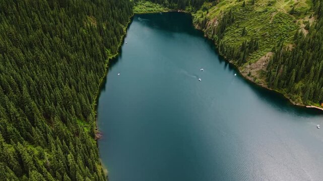 Cinematic drone pan up from glacial waters of Kolsay lake to the high altitude mountain peaks through the valley in Kazakhstan