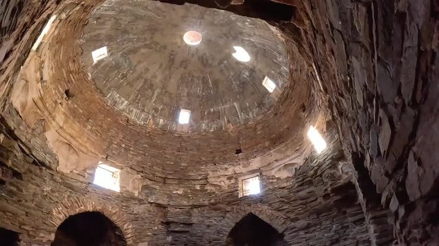 Interior view of the central domed chamber inside the medieval Tash Rabat caravanserai in Kyrgyzstan. Ancient stone architecture featuring the massive dome, skylight openings, arched doorways.