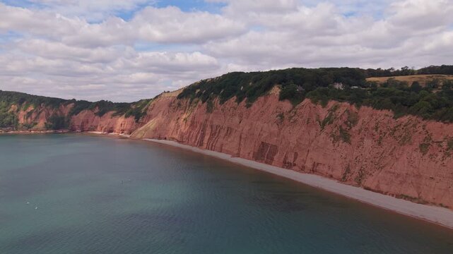 Aerial drone footage of the striking red sandstone cliffs at Jacob's Ladder Beach in Sidmouth, East Devon, England. The video captures the Jurassic Coast, dramatic coastal scenery, and the English Cha