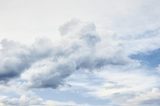Dramatic expansive cloudscape fills sky with towering cumulus formations, soft sunlight, subtle blue tones, evoking calm, wonder and moody atmospheric feeling ideal for backgrounds and nature projects