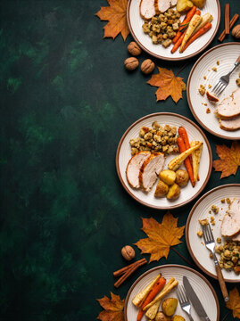 Multiple plates of roast poultry dinner with vegetables on a dark green background with copy space. Thanksgiving and Christmas family meal concept.