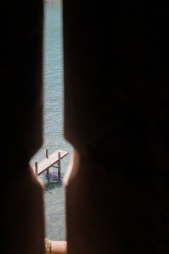 Scenic view of a wooden pier on Lake Geneva through a historic stone arrow slit inside Chillon Castle, Switzerland.
Medieval castle loophole window framing a tranquil turquoise lake and wooden dock, 
